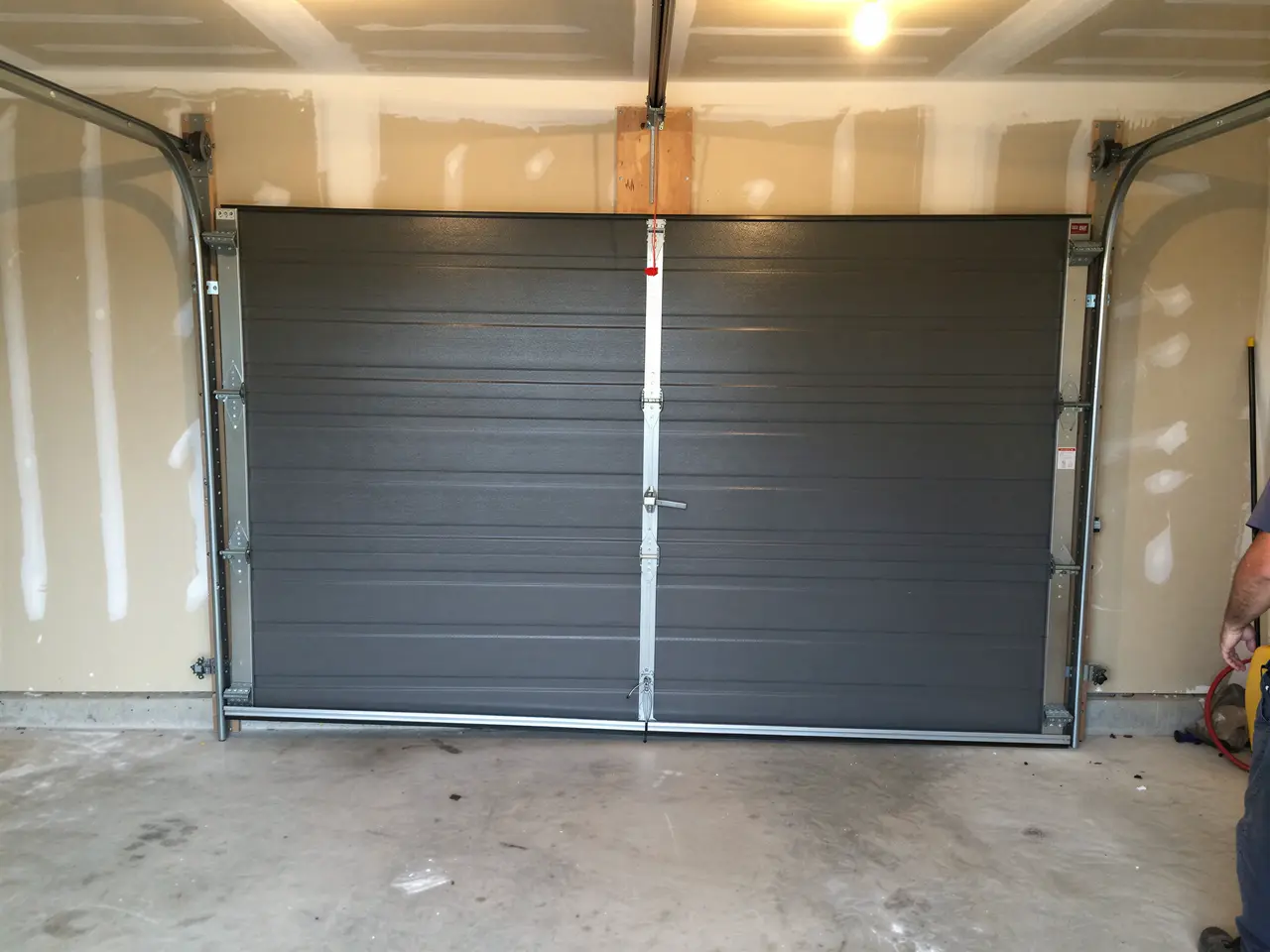 A new gray garage door is installed in an unfinished garage.